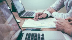 Deux personnes travaillent sur des documents avec des ordinateurs portables, image utilisée pour illustrer l’organisation des dossiers partagés en TPE.